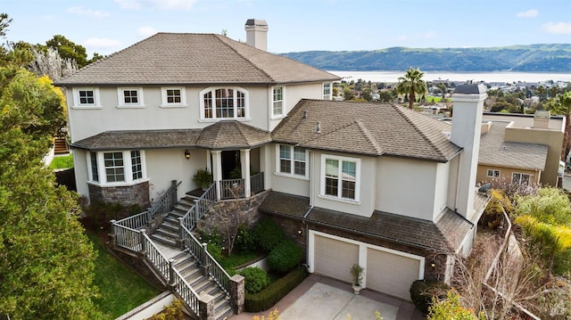 view of front of house with a chimney, stucco siding, a garage, a water and mountain view, and concrete driveway