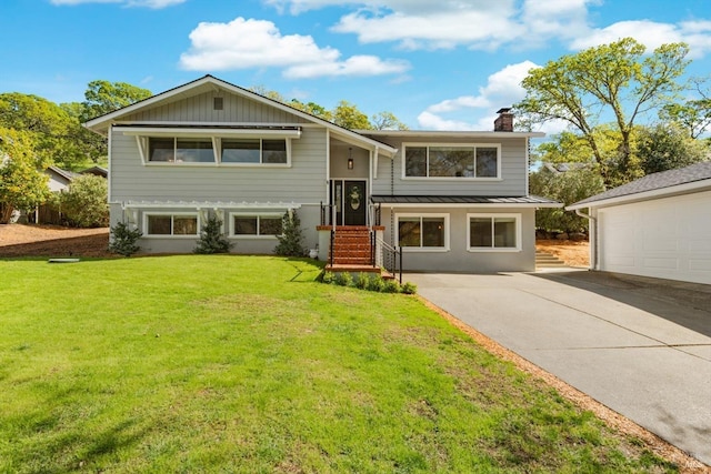 raised ranch featuring a front lawn, a standing seam roof, a chimney, metal roof, and concrete driveway