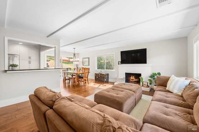 living room featuring a brick fireplace, wood finished floors, visible vents, and baseboards