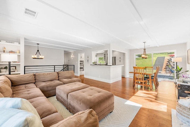 living area featuring beamed ceiling, visible vents, light wood finished floors, and a notable chandelier