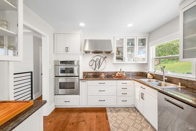 kitchen with a sink, extractor fan, glass insert cabinets, light wood finished floors, and appliances with stainless steel finishes