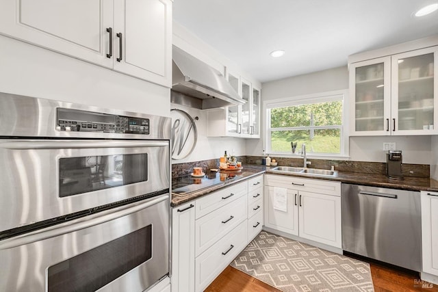 kitchen with a sink, dark countertops, extractor fan, white cabinetry, and appliances with stainless steel finishes