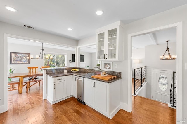 kitchen with white cabinets, a peninsula, light wood-type flooring, visible vents, and glass insert cabinets
