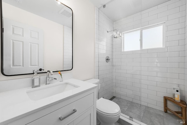 full bathroom featuring a tile shower, toilet, vanity, and visible vents