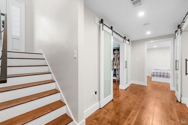 hall with visible vents, recessed lighting, light wood-style floors, and a barn door