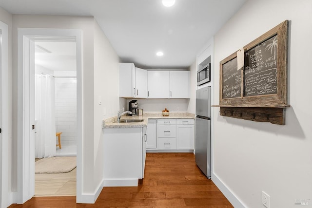 kitchen with white cabinets, wood finished floors, a sink, and appliances with stainless steel finishes