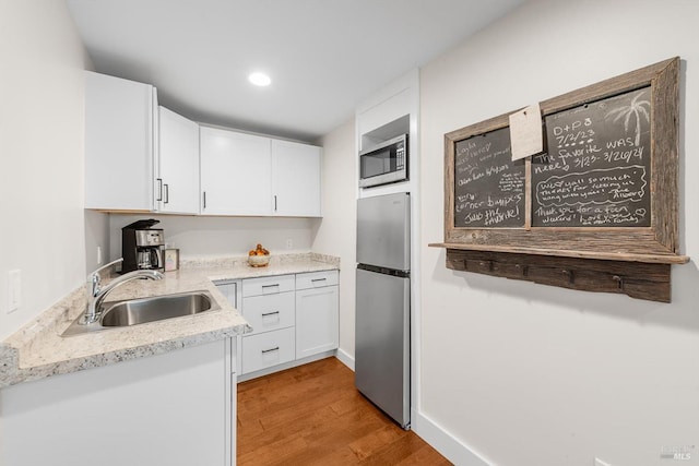 kitchen featuring light wood-type flooring, white cabinetry, stainless steel appliances, and a sink