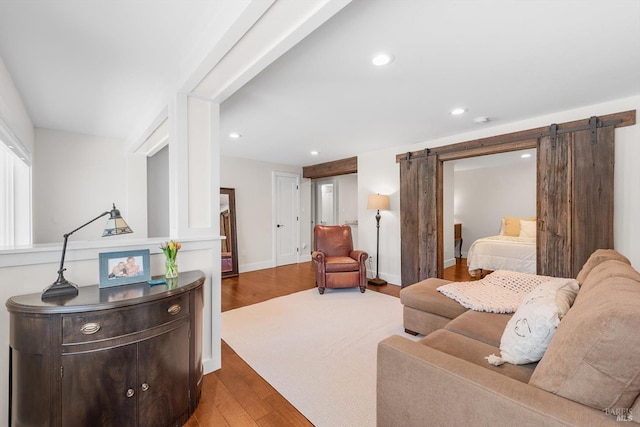 living area featuring a barn door, baseboards, wood finished floors, and recessed lighting