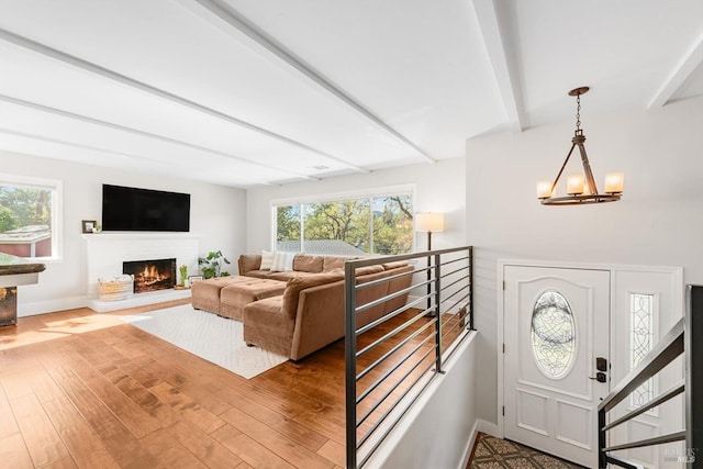living area featuring beamed ceiling, plenty of natural light, wood finished floors, and an inviting chandelier