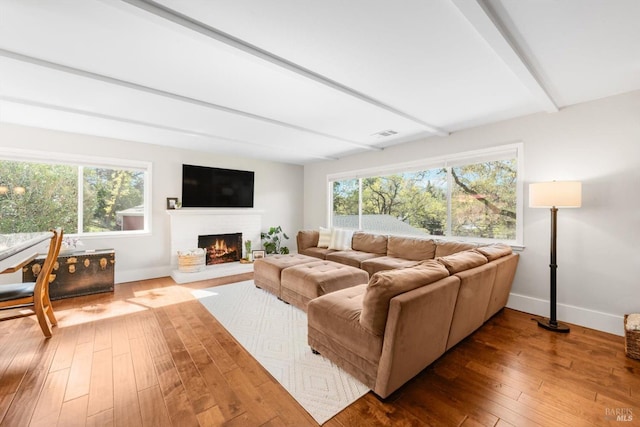 living area with visible vents, beamed ceiling, baseboards, a fireplace, and hardwood / wood-style flooring