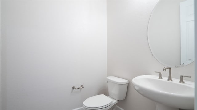 half bath featuring baseboards, a sink, and toilet