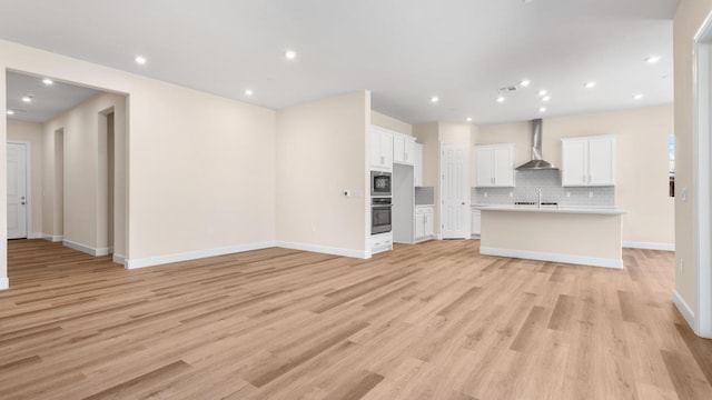 unfurnished living room with light wood-style floors, a sink, baseboards, and recessed lighting