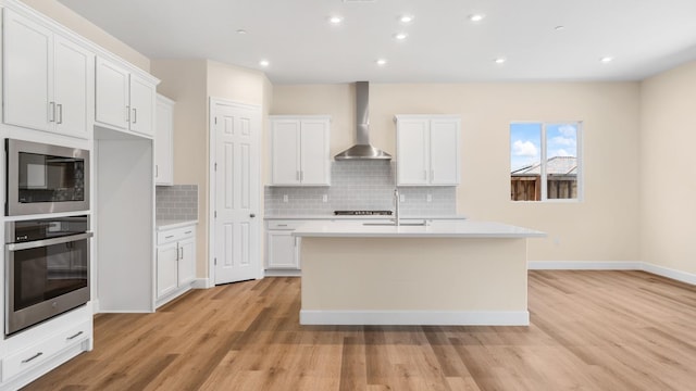 kitchen featuring wall chimney range hood, oven, a sink, light wood-style floors, and built in microwave