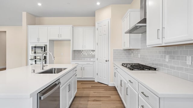 kitchen featuring white cabinetry, appliances with stainless steel finishes, a sink, and wall chimney exhaust hood