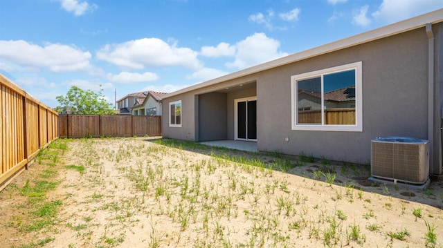 rear view of house featuring central AC, a fenced backyard, and stucco siding