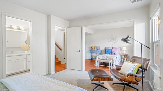 bedroom with visible vents, baseboards, light colored carpet, ensuite bath, and a sink