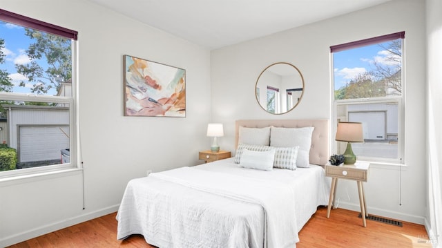 bedroom with baseboards, multiple windows, visible vents, and wood finished floors