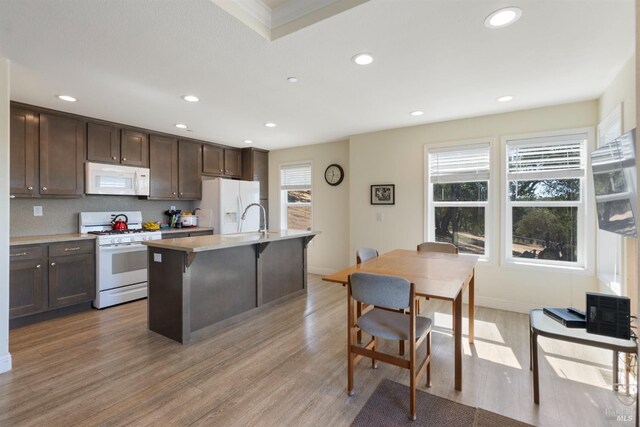 kitchen with dark brown cabinets, light countertops, light wood-style flooring, white appliances, and a kitchen island with sink