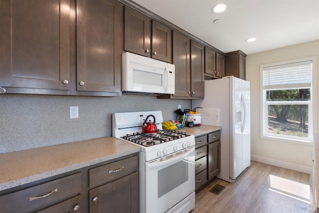 kitchen featuring white appliances, light stone countertops, light wood finished floors, dark brown cabinets, and tasteful backsplash