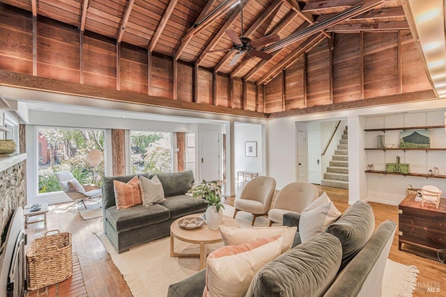 living area with wood ceiling, a ceiling fan, beam ceiling, light wood-type flooring, and stairs