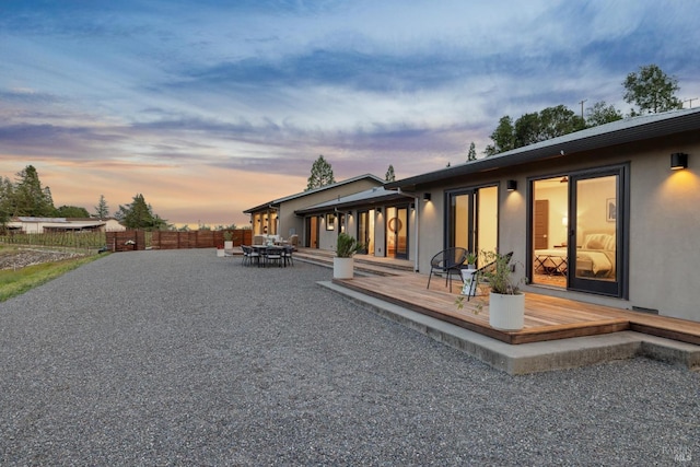 back of property featuring stucco siding, outdoor dining space, a wooden deck, and fence