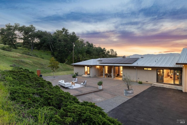 rear view of house with a patio, stucco siding, an outdoor hangout area, metal roof, and solar panels