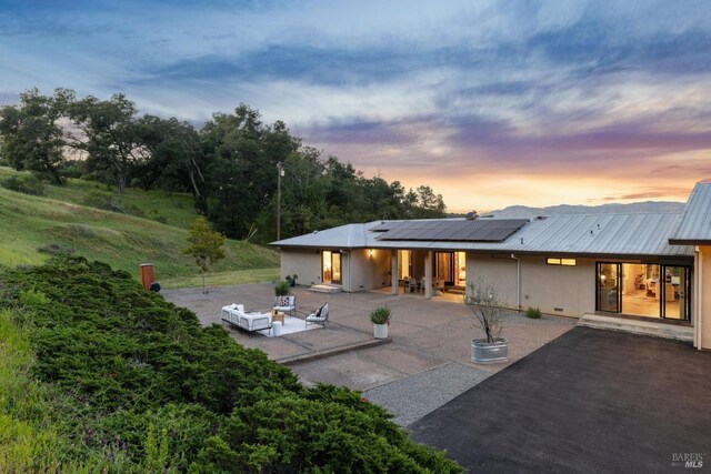 4127 Dry Creek Rd, Napa, CA 94558 - back of house at dusk with a patio area, solar panels, metal roof, outdoor lounge area, and stucco siding