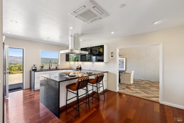 kitchen with a sink, dark countertops, dark wood-style flooring, and island range hood