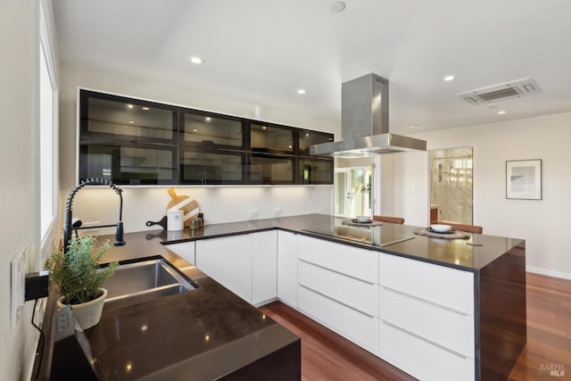 kitchen featuring island exhaust hood, visible vents, dark countertops, modern cabinets, and a sink