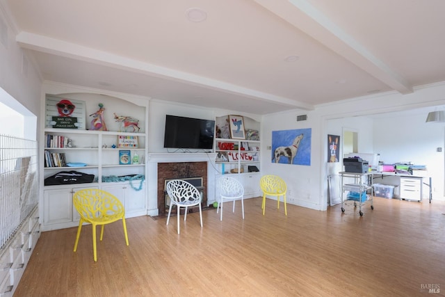 living area featuring built in features, beam ceiling, light wood-style floors, and a fireplace