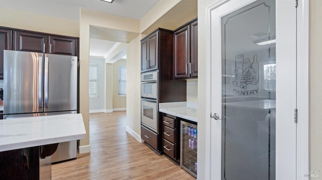 kitchen with beverage cooler, stainless steel appliances, dark brown cabinetry, light wood finished floors, and light stone countertops