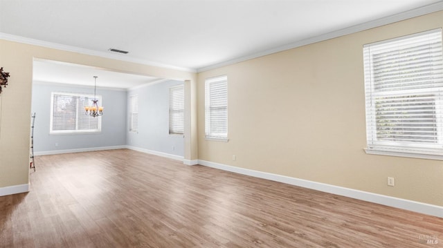 spare room with visible vents, wood finished floors, an inviting chandelier, crown molding, and baseboards