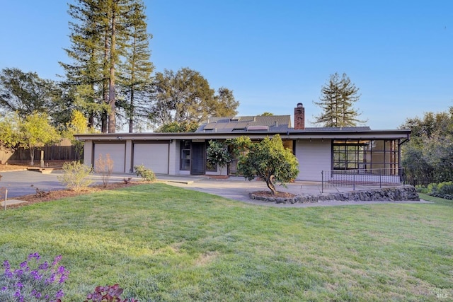 view of front of property with fence, driveway, a front lawn, a garage, and roof mounted solar panels