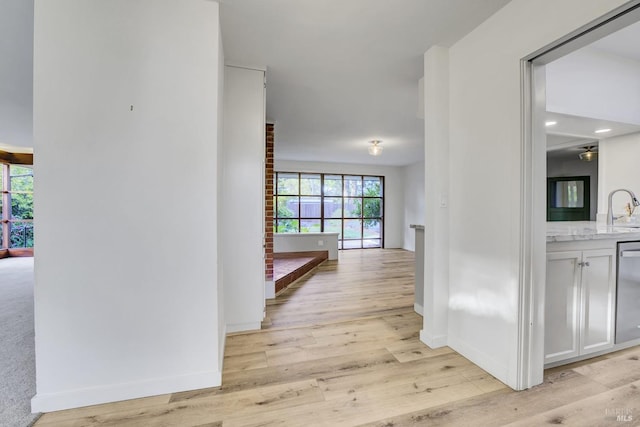 corridor with light wood-style flooring, baseboards, and a sink
