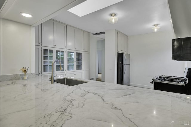 kitchen featuring a sink, light stone counters, appliances with stainless steel finishes, and a skylight