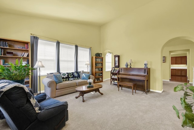 living area featuring a towering ceiling, baseboards, arched walkways, and carpet floors