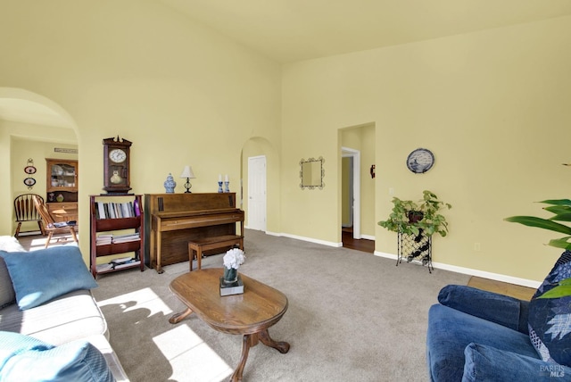 living area featuring a high ceiling, carpet, arched walkways, and baseboards