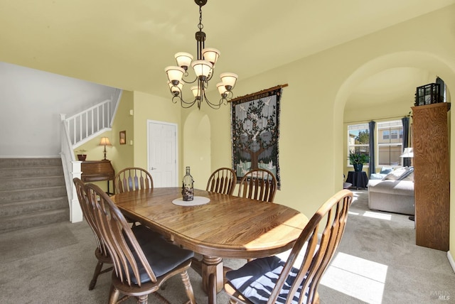 carpeted dining area featuring stairway, arched walkways, and a chandelier