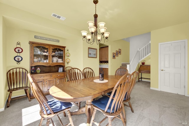 dining space featuring visible vents, baseboards, an inviting chandelier, stairs, and light colored carpet
