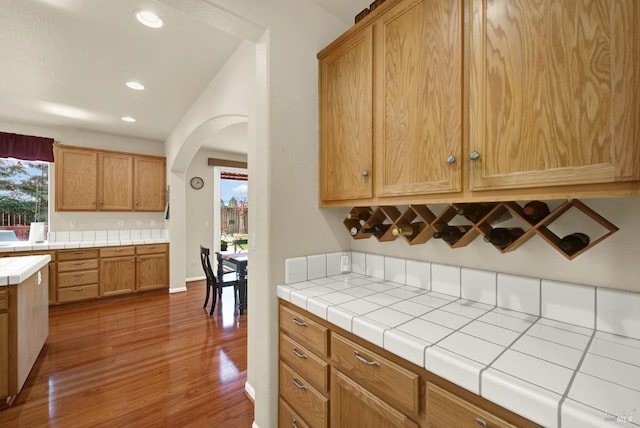 kitchen with arched walkways, a healthy amount of sunlight, wood finished floors, and tile counters