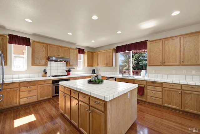 kitchen featuring stainless steel oven, under cabinet range hood, dark wood-style flooring, and a sink