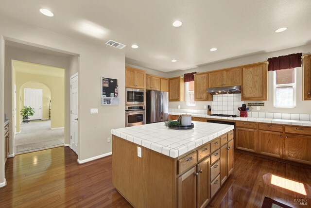 kitchen featuring visible vents, arched walkways, dark wood-type flooring, under cabinet range hood, and appliances with stainless steel finishes