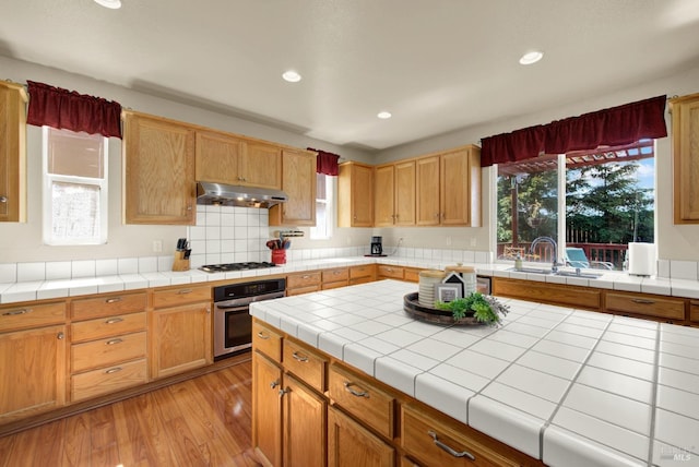 kitchen featuring under cabinet range hood, a sink, light wood-style floors, stainless steel oven, and white gas stovetop