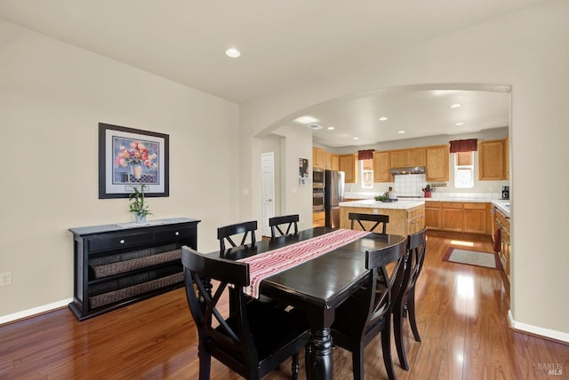 dining area featuring arched walkways, baseboards, and wood finished floors