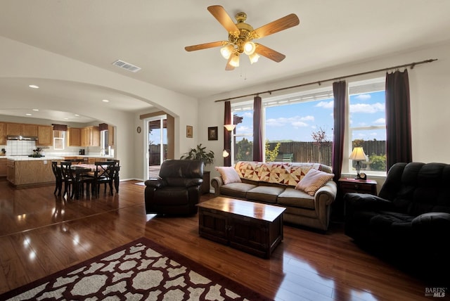 living room with ceiling fan, visible vents, arched walkways, and dark wood finished floors