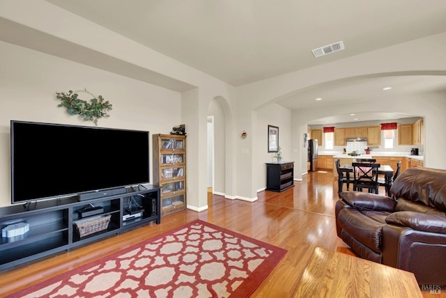 living area with visible vents, baseboards, light wood-type flooring, recessed lighting, and arched walkways
