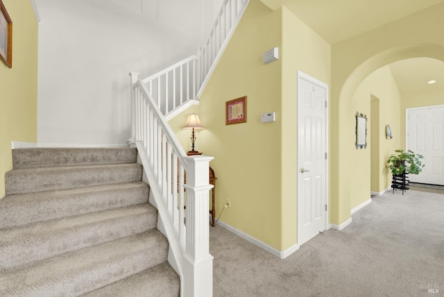 stairway featuring arched walkways, baseboards, and carpet floors