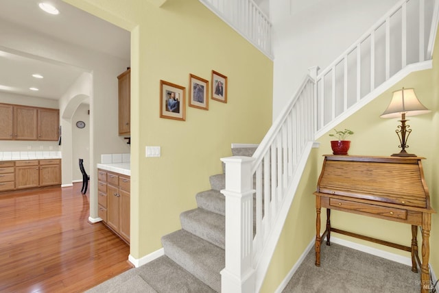 stairs with arched walkways, recessed lighting, baseboards, and wood finished floors