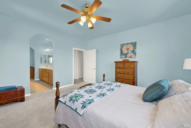bedroom featuring a sink, arched walkways, baseboards, light colored carpet, and ceiling fan