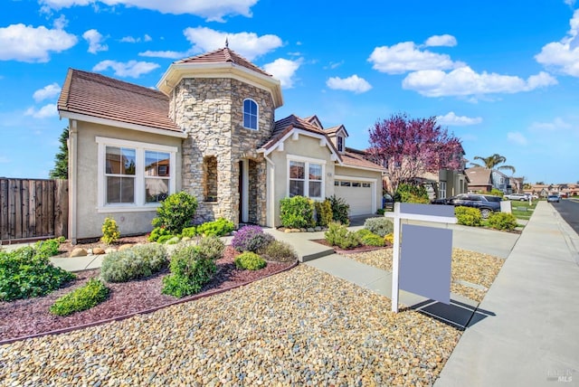 view of front of home featuring stucco siding, a tile roof, stone siding, fence, and an attached garage